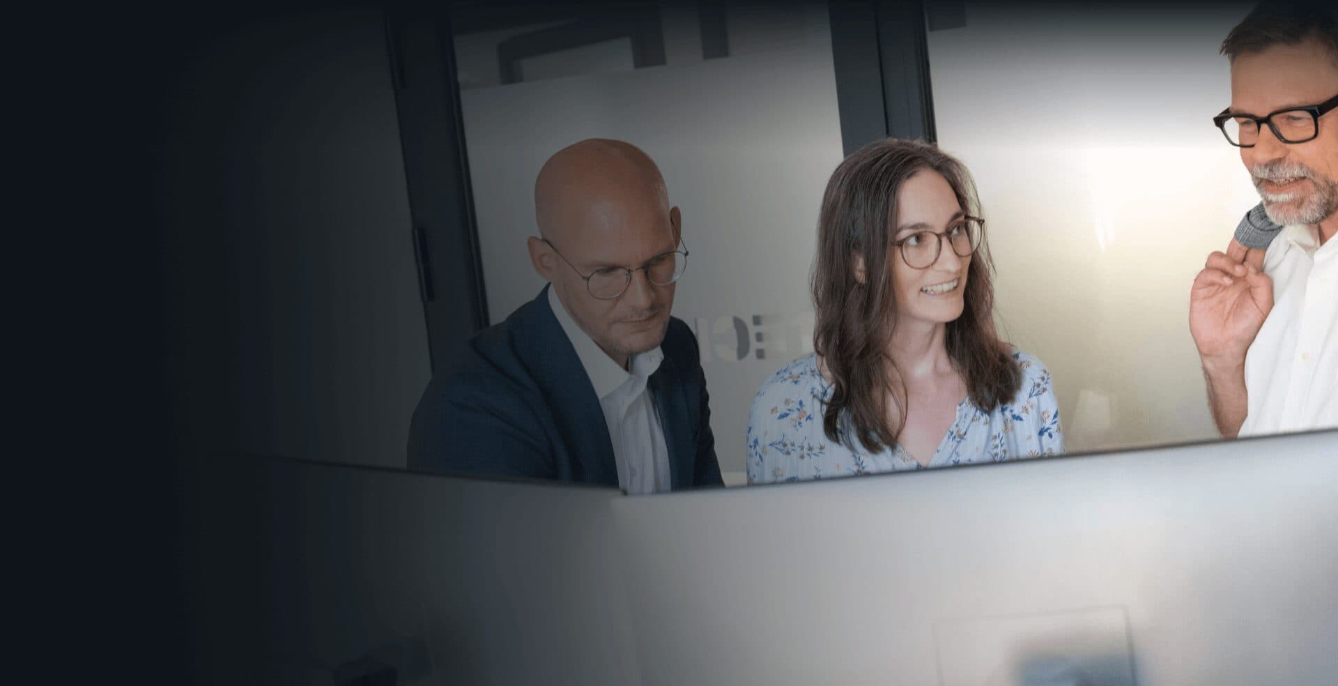Beratungsteam blickt im Büro gemeinsam auf einen Monitor und bespricht den KI-Einsatz