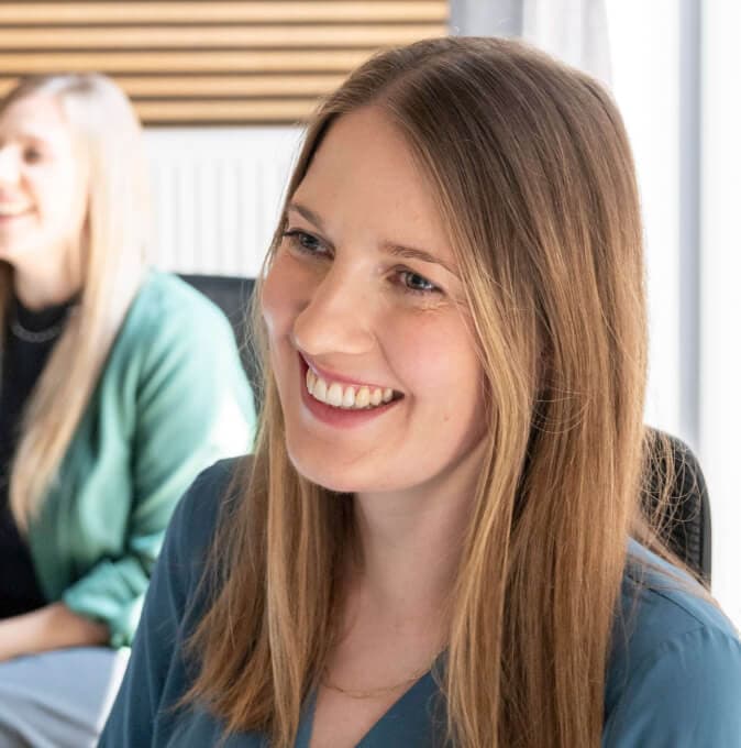 Lächelnde Teilnehmerin einer KI-Schulung, im Hintergrund eine Kollegin