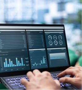 Hände tippen auf einem Laptop mit Dashboard aus Balkendiagrammen und Kennzahlen